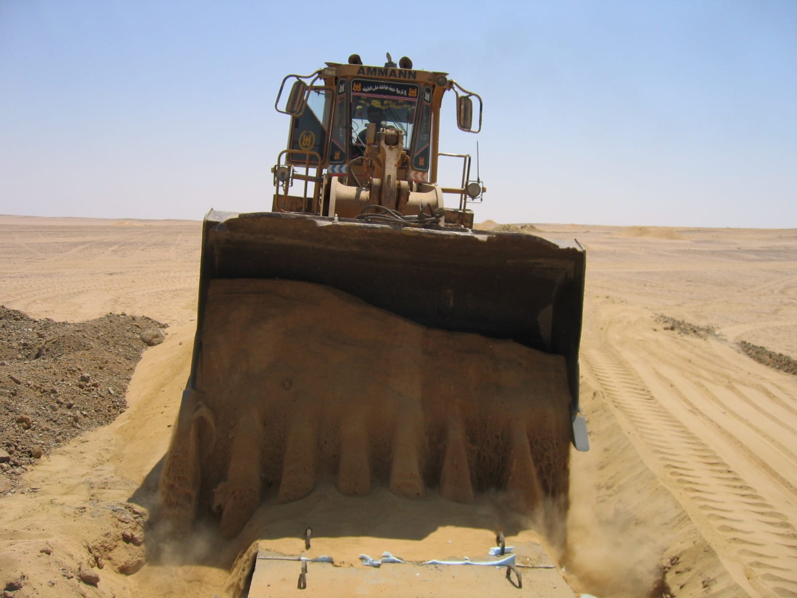A heavy dozer moving sand at a desert work location.